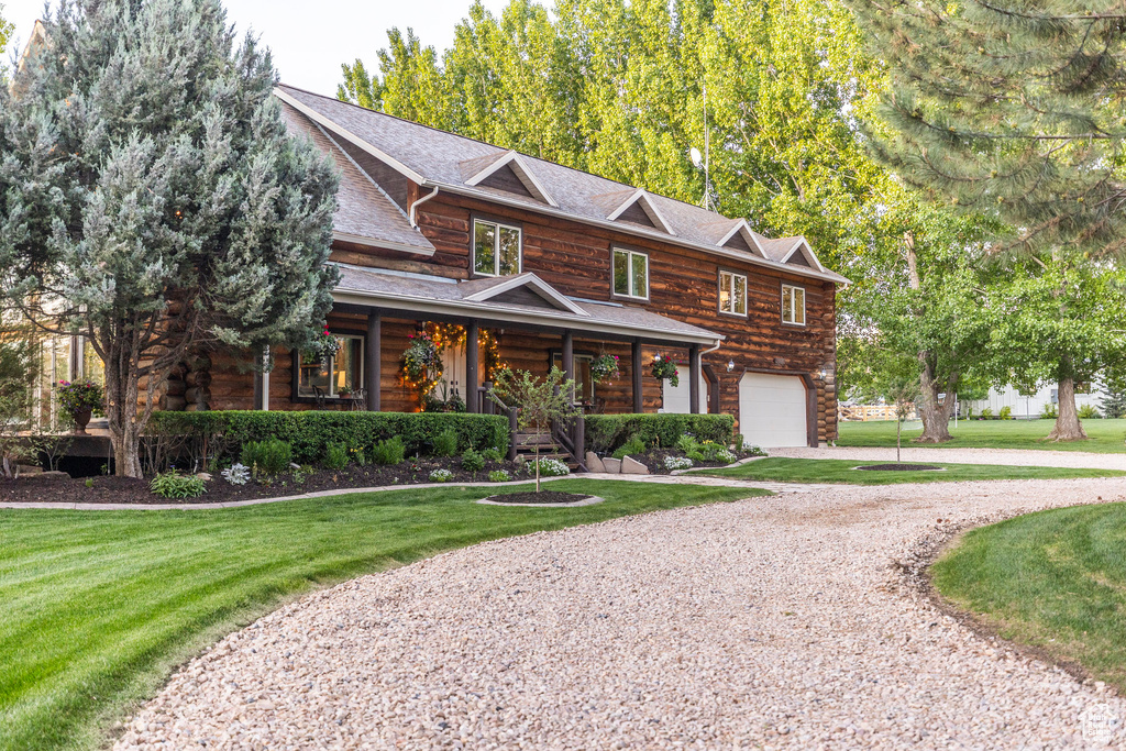 View of front of home with covered porch, gravel driveway, a garage, and a front lawn