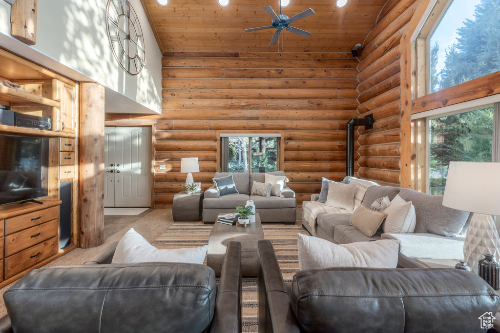Carpeted living room featuring high vaulted ceiling, log walls, wooden ceiling, plenty of natural light, and ceiling fan