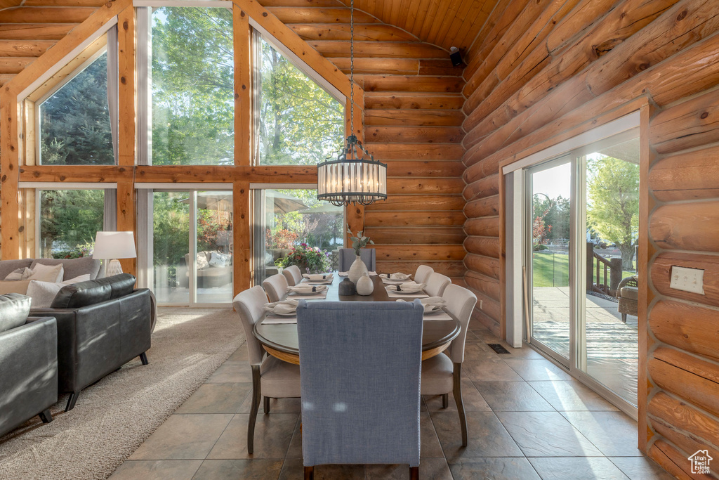 Dining space with plenty of natural light, a chandelier, wood ceiling, rustic walls, and high vaulted ceiling