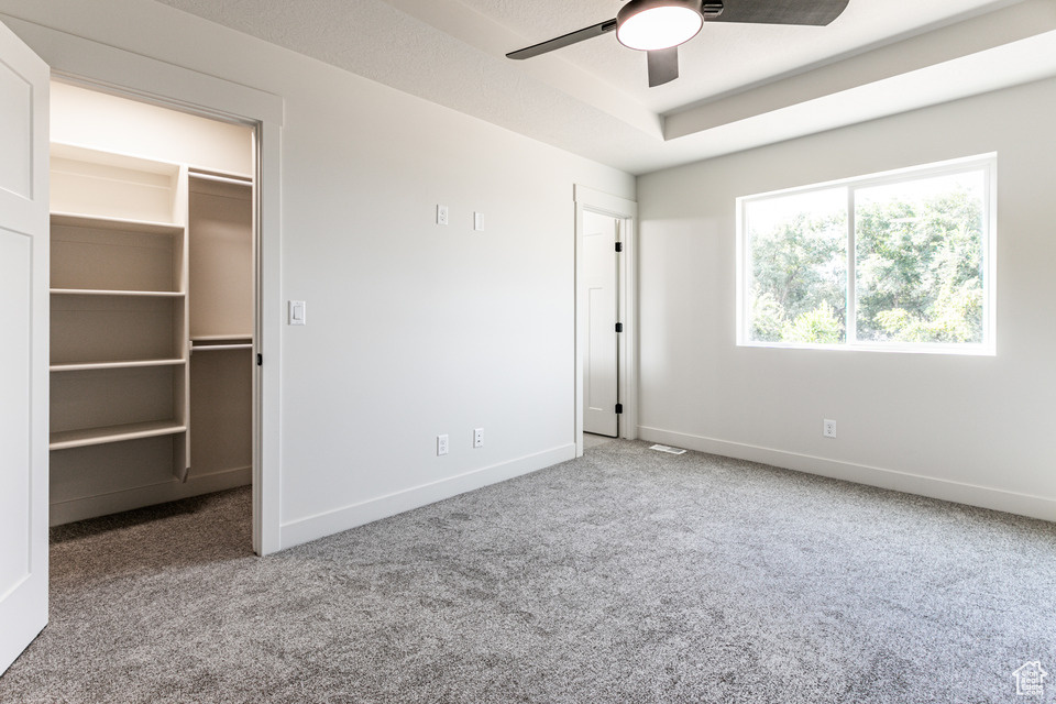 Unfurnished bedroom featuring a spacious closet, a closet, carpet floors, and ceiling fan