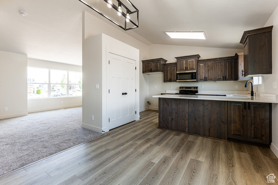 Kitchen with range, sink, light colored carpet, dark brown cabinetry, and lofted ceiling