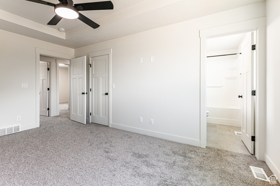 Unfurnished bedroom with ensuite bathroom, ceiling fan, and light colored carpet