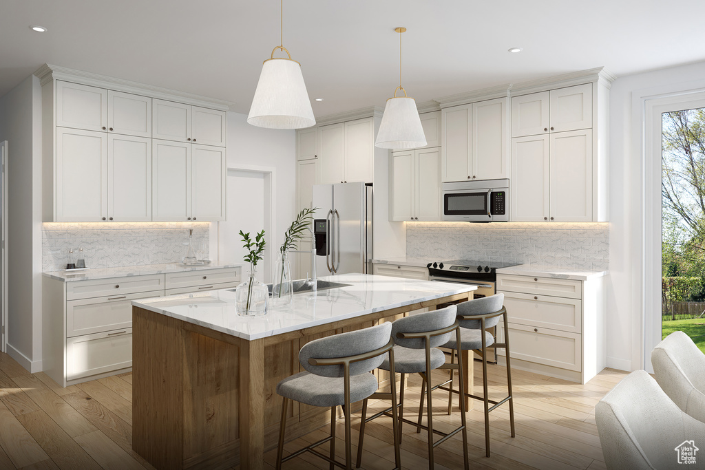 Kitchen with backsplash, appliances with stainless steel finishes, an island with sink, and pendant lighting