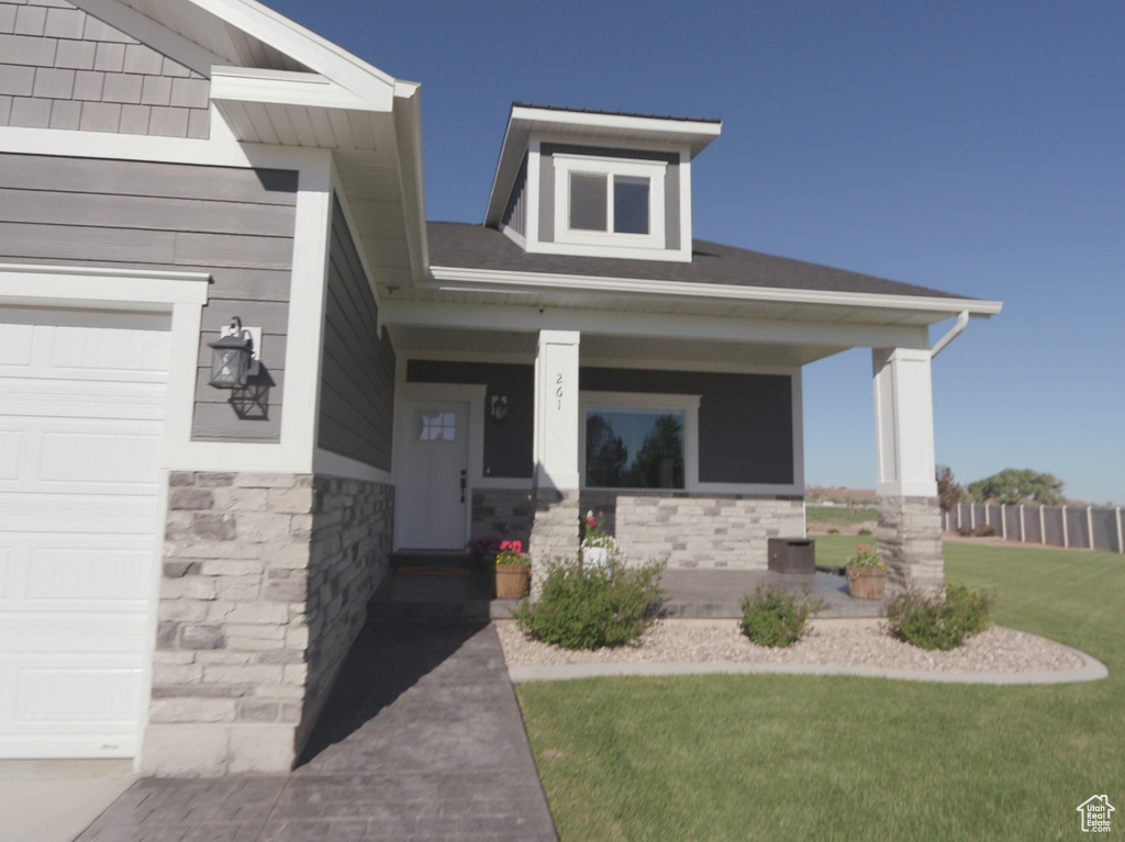 View of exterior entry with a porch, a lawn, and a garage