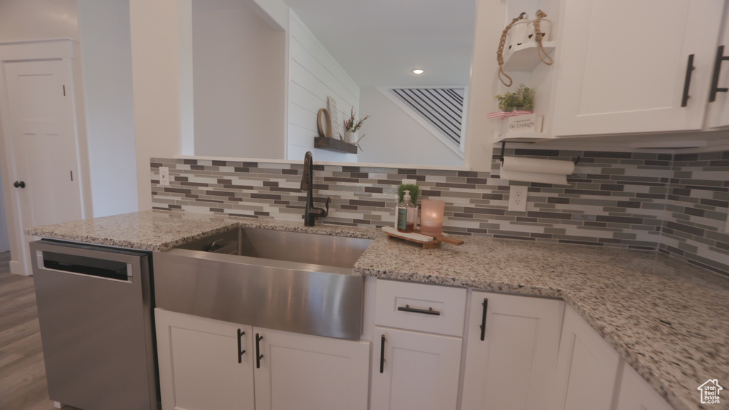 Kitchen featuring white cabinetry, light stone countertops, hardwood / wood-style floors, backsplash, and dishwasher