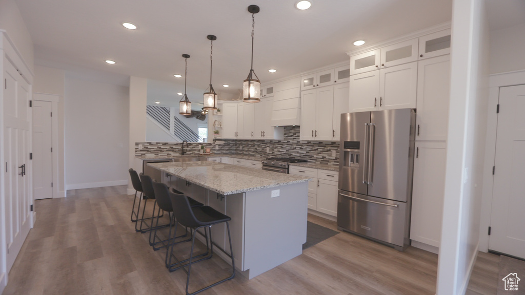Kitchen with wood-type flooring, white cabinetry, premium appliances, and tasteful backsplash