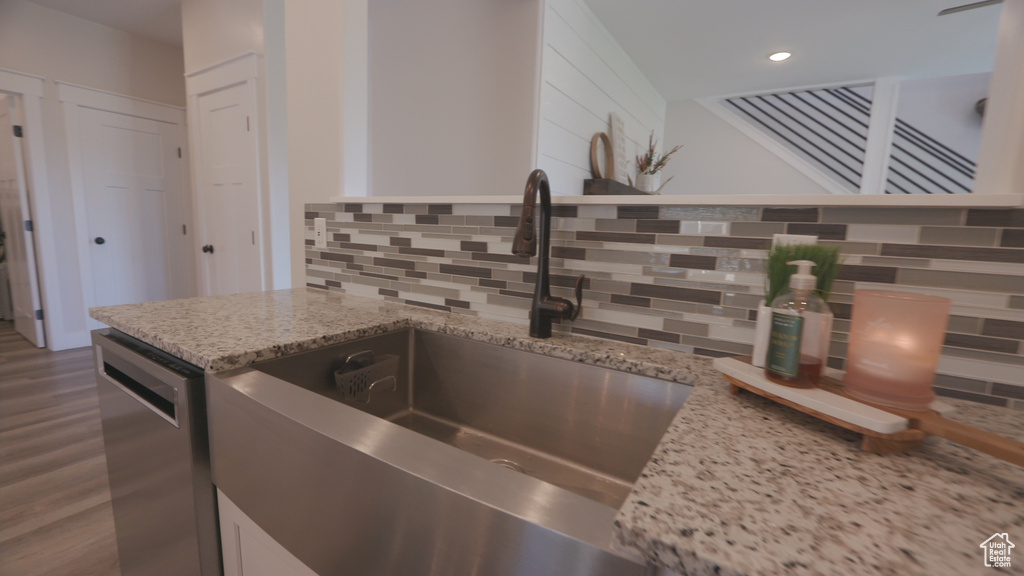 Kitchen featuring sink, dishwasher, light stone counters, and tasteful backsplash