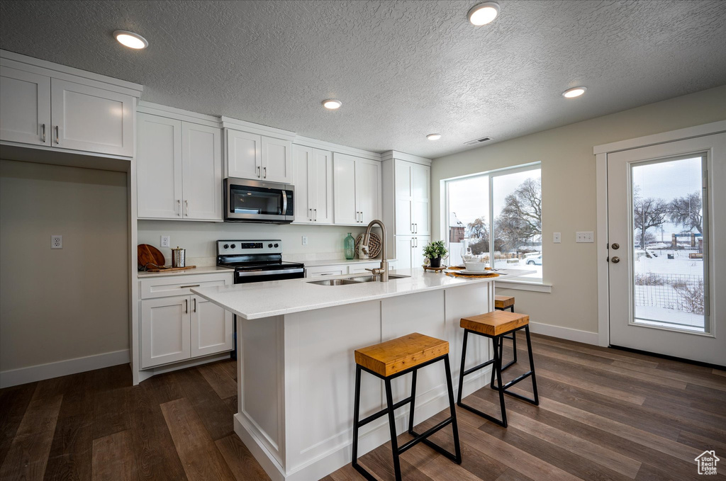 Kitchen featuring appliances with stainless steel finishes, white cabinets, a kitchen island with sink, and dark wood-type flooring