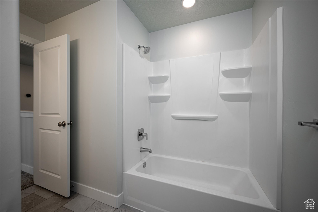 Bathroom with tile flooring, washtub / shower combination, and a textured ceiling