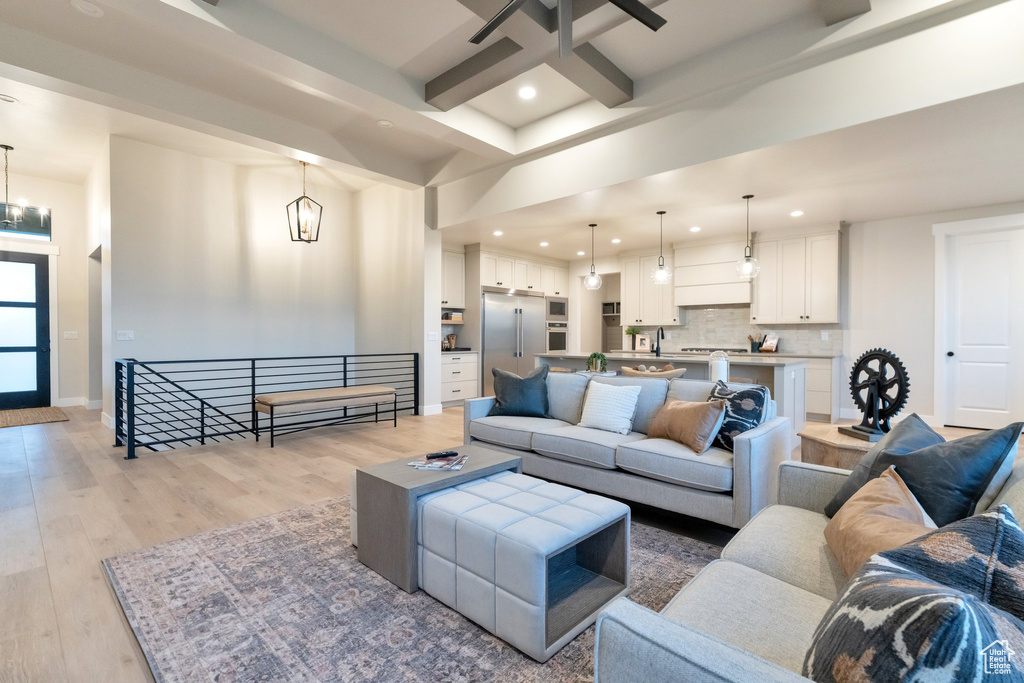 Living room featuring beamed ceiling, coffered ceiling, light wood-type flooring, and ceiling fan with notable chandelier