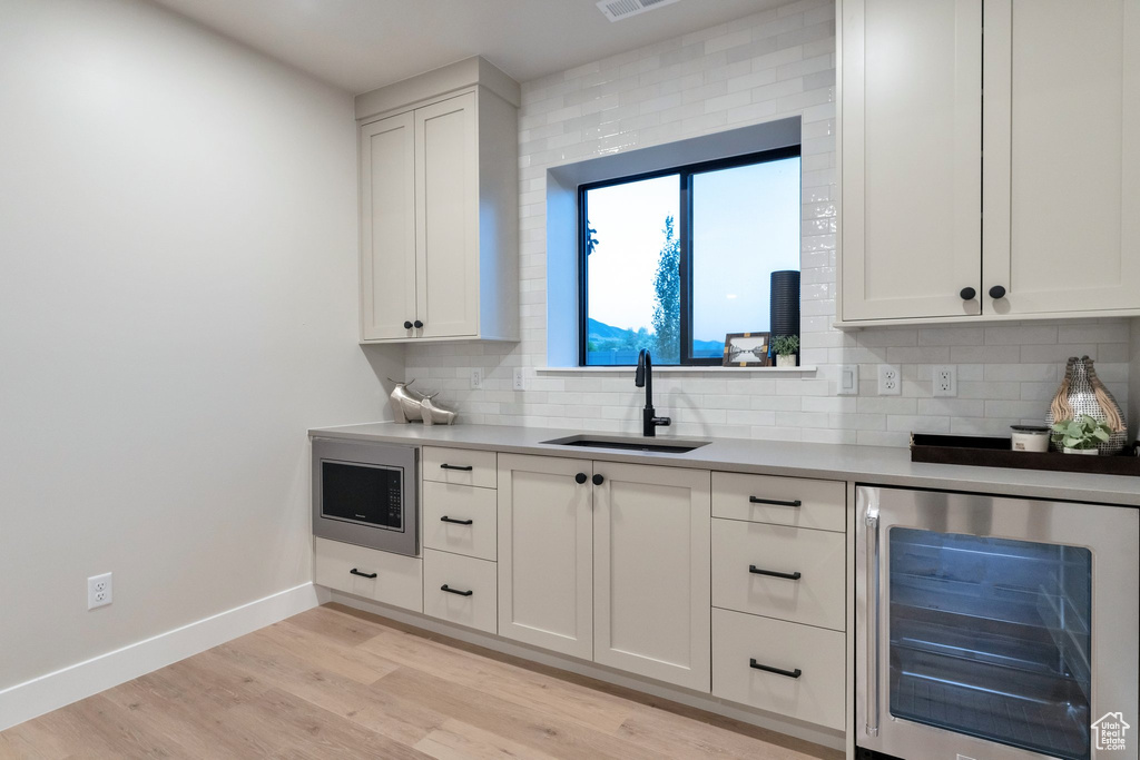 Kitchen featuring backsplash, stainless steel microwave, light hardwood / wood-style flooring, and beverage cooler