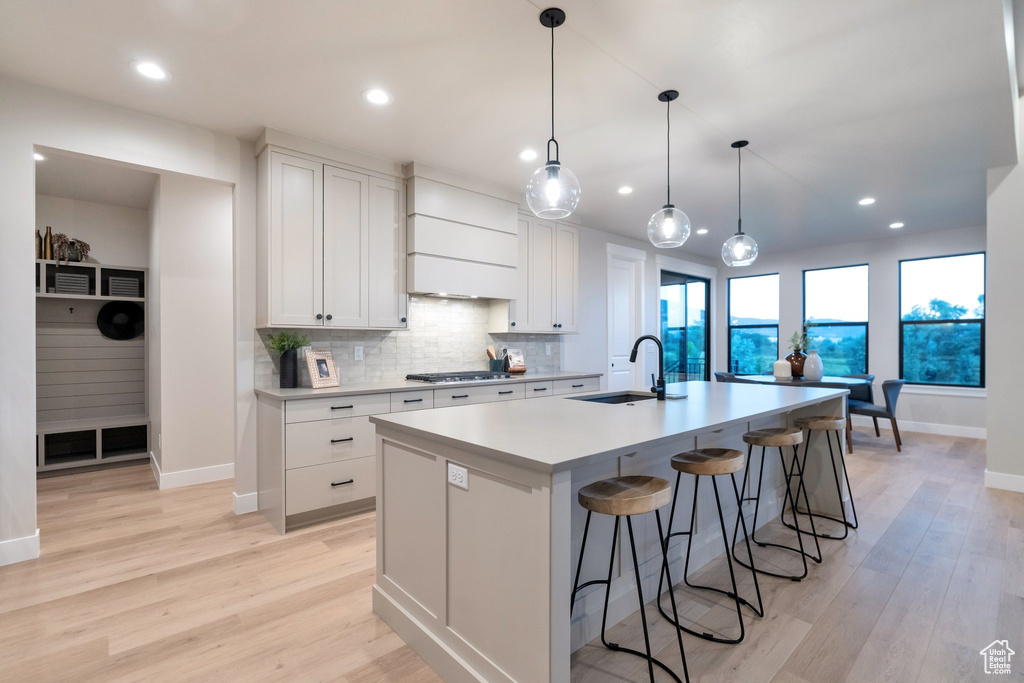 Kitchen with tasteful backsplash, a center island with sink, light wood-type flooring, sink, and white cabinetry