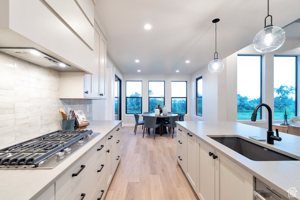 Kitchen with light hardwood / wood-style flooring, pendant lighting, backsplash, sink, and white cabinetry