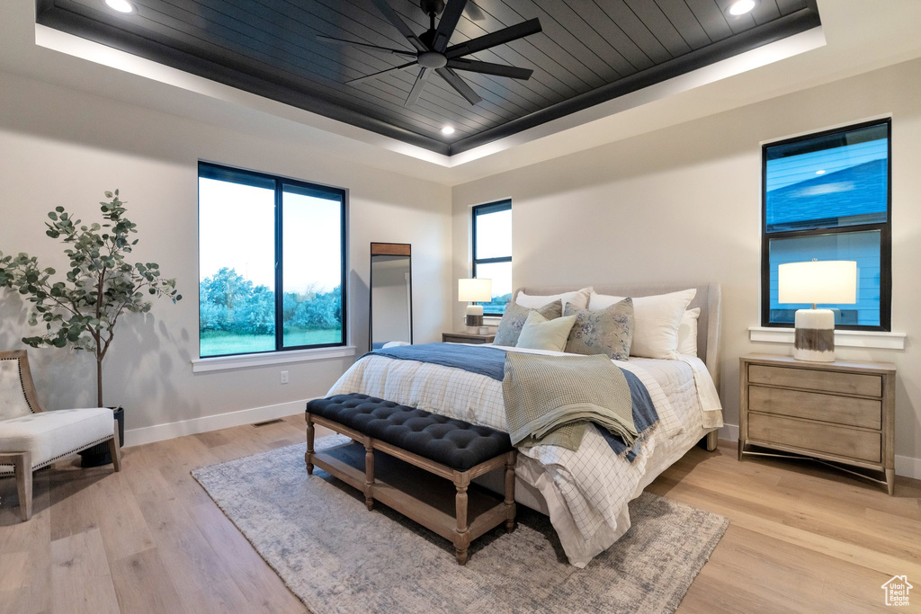 Bedroom with ceiling fan, a raised ceiling, and light hardwood / wood-style floors