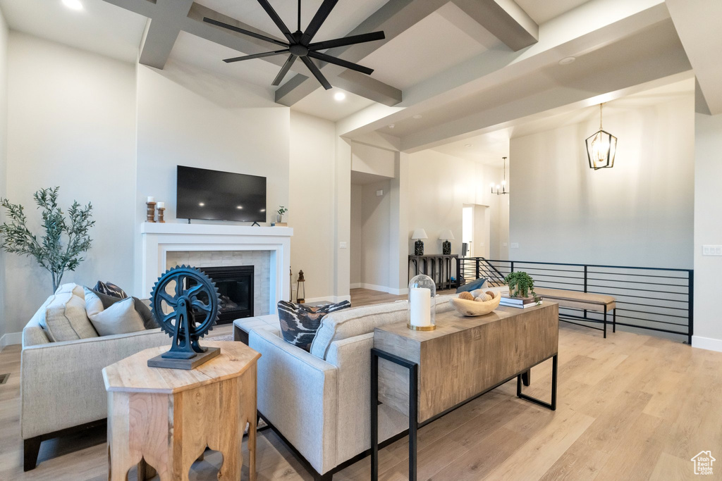 Living room with beamed ceiling, a tiled fireplace, light hardwood / wood-style floors, and ceiling fan with notable chandelier