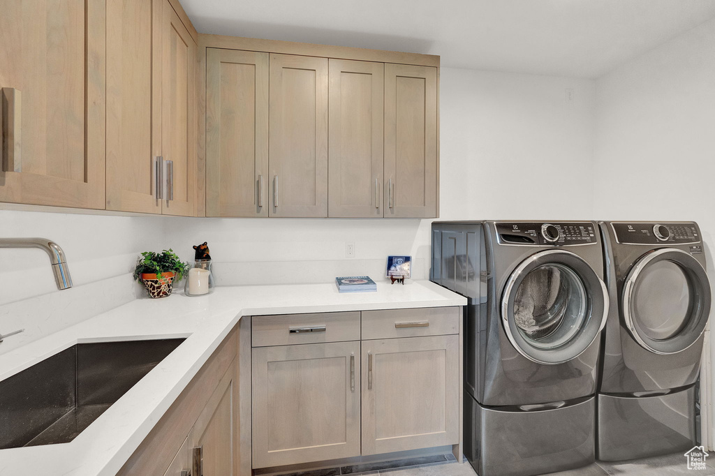 Clothes washing area featuring cabinets, sink, and washing machine and dryer