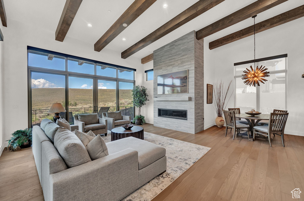 Living room featuring beamed ceiling, a fireplace, an inviting chandelier, and light hardwood / wood-style flooring