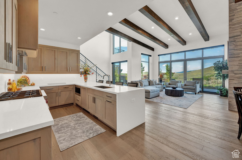 Kitchen with beamed ceiling, sink, light hardwood / wood-style flooring, and kitchen peninsula