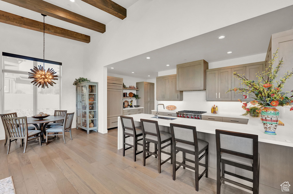 Kitchen featuring hanging light fixtures, light hardwood / wood-style flooring, beam ceiling, sink, and a kitchen bar