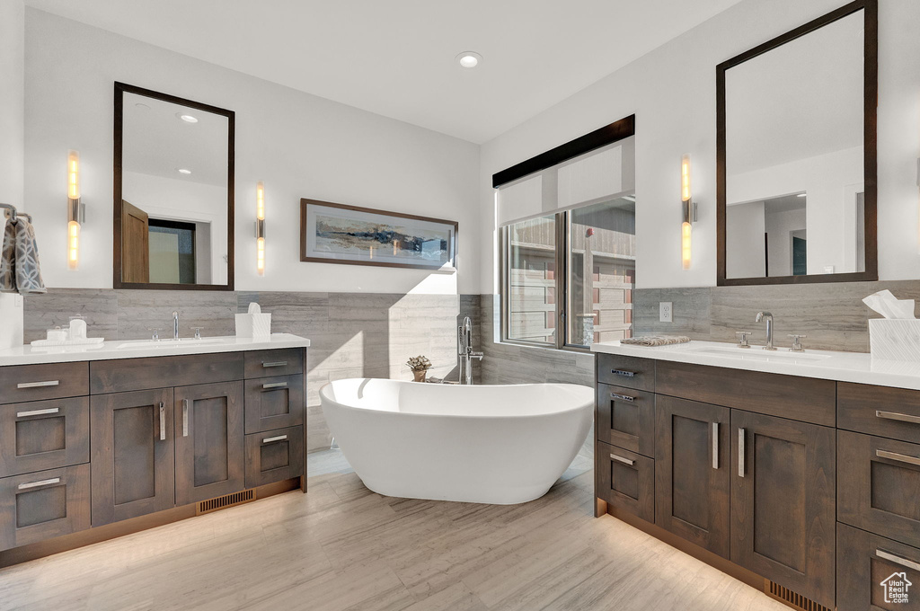 Bathroom featuring double sink vanity, tile walls, tasteful backsplash, and a bathing tub