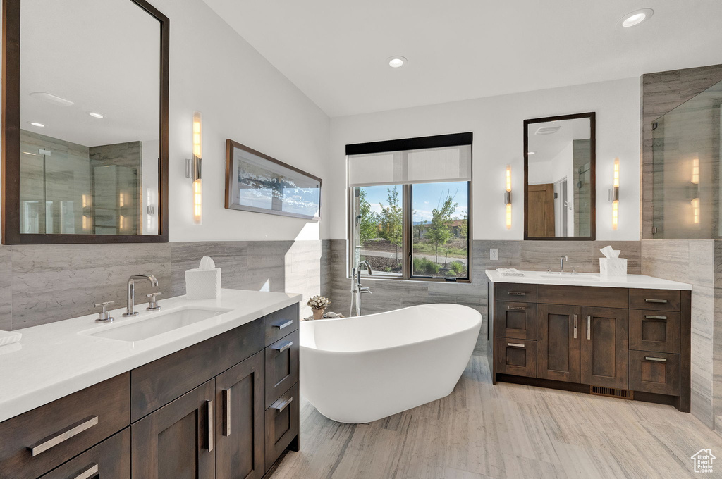 Bathroom with tile walls, double sink vanity, and a bath to relax in