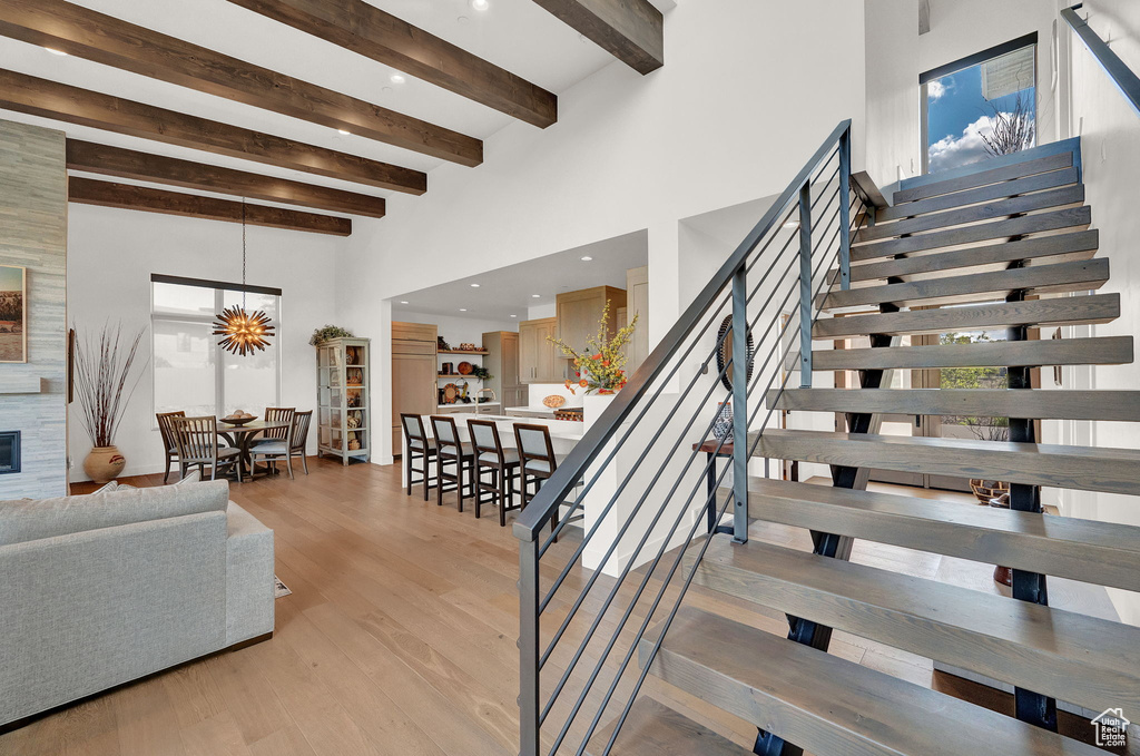 Stairway with a high ceiling, beamed ceiling, light hardwood / wood-style floors, and a chandelier