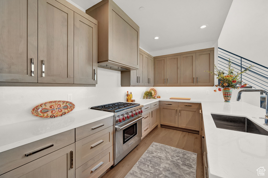 Kitchen featuring premium range hood, sink, luxury range, and light hardwood / wood-style flooring