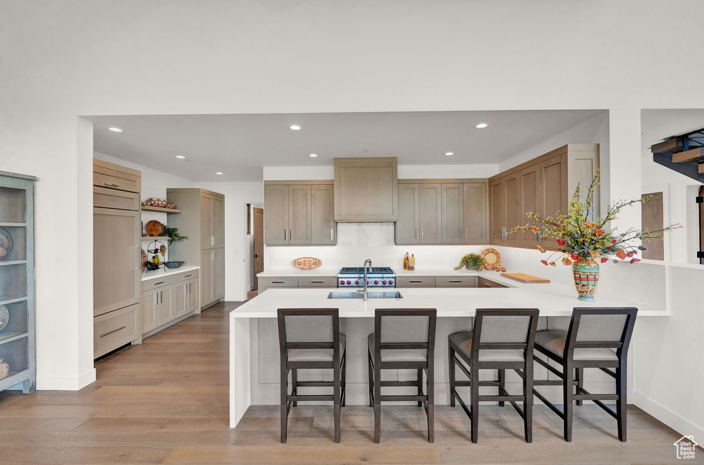 Kitchen featuring custom range hood, light hardwood / wood-style flooring, kitchen peninsula, a kitchen bar, and sink