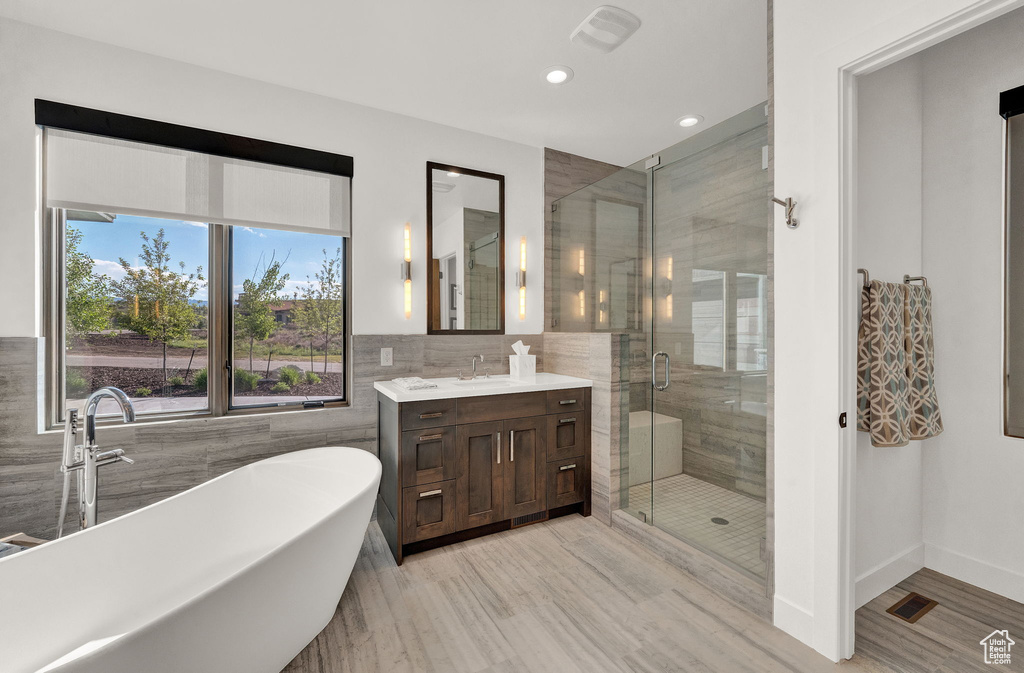 Bathroom featuring shower with separate bathtub, tile walls, and large vanity