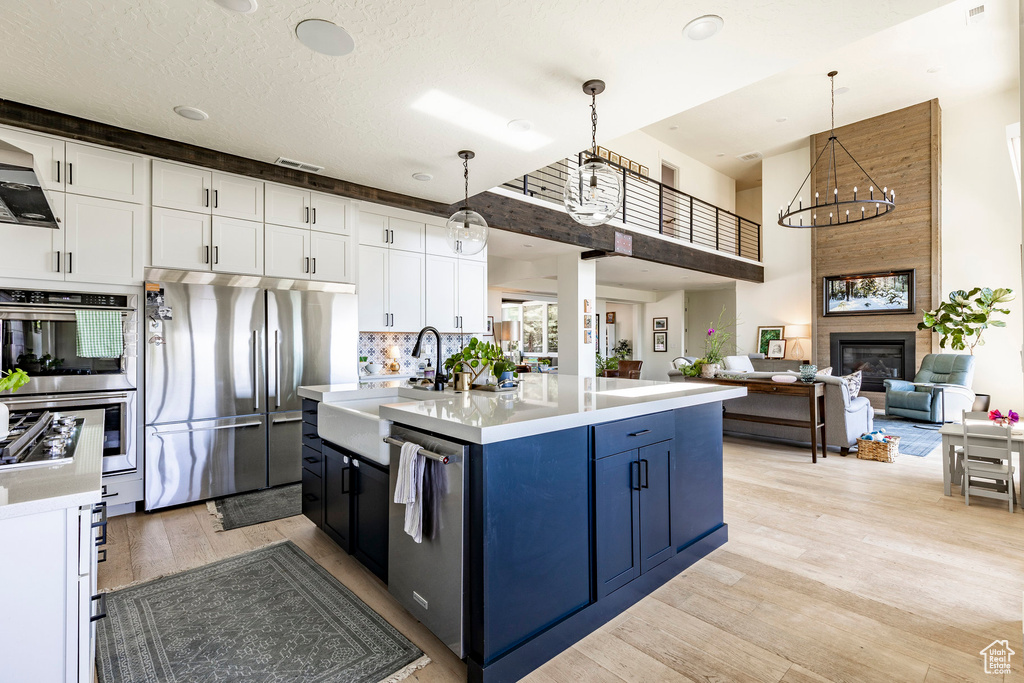 Kitchen with stainless steel appliances, light hardwood / wood-style floors, a kitchen island with sink, and white cabinetry