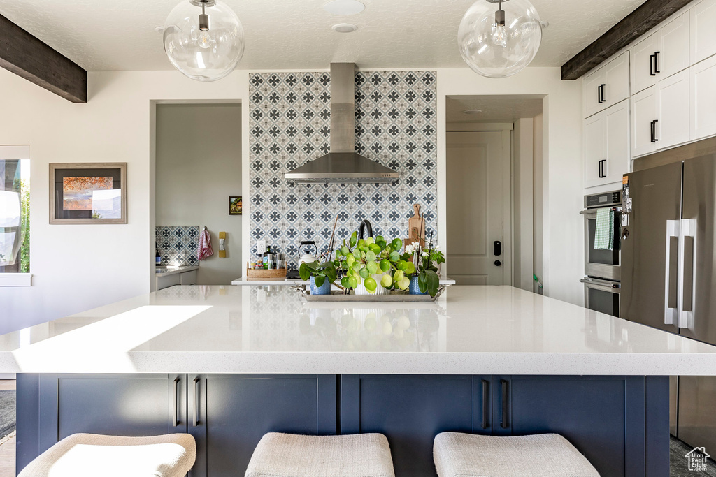 Kitchen featuring beam ceiling, pendant lighting, a breakfast bar, and wall chimney exhaust hood