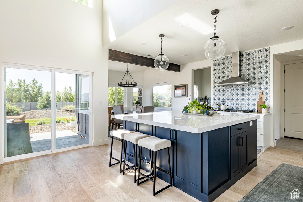 Kitchen featuring wall chimney range hood, a center island, light hardwood / wood-style floors, and pendant lighting