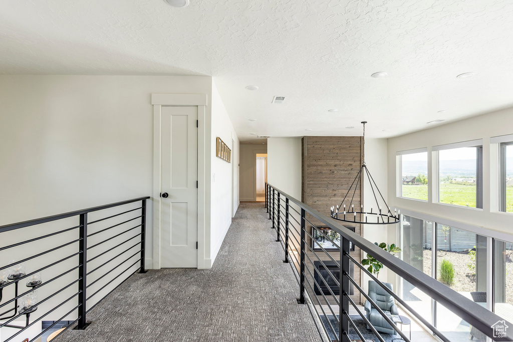 Corridor with carpet floors, a textured ceiling, and a chandelier