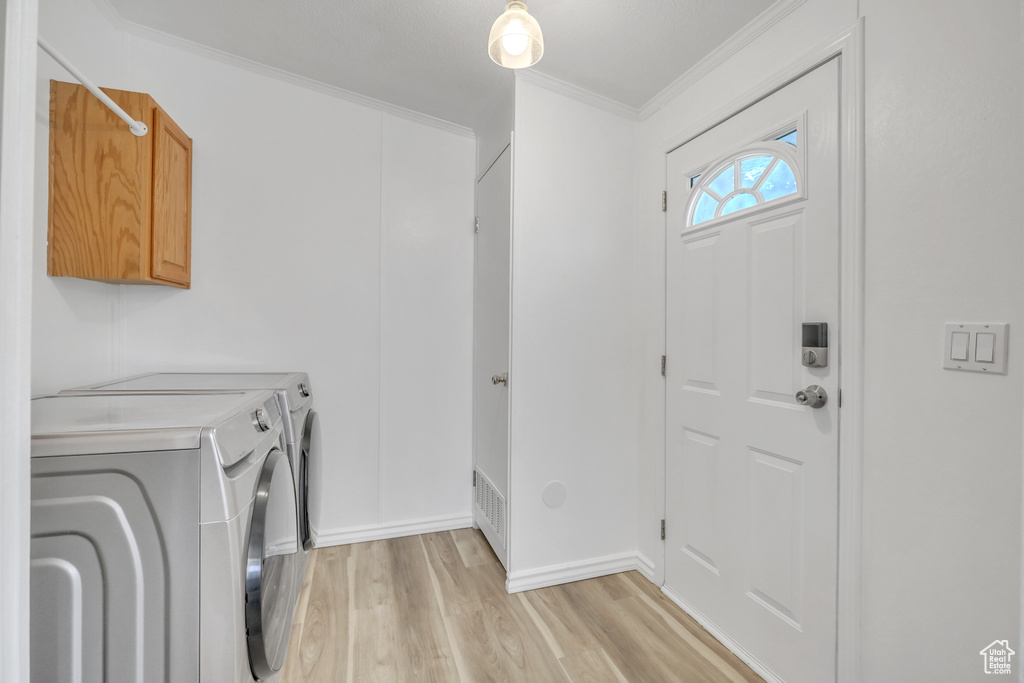 Clothes washing area featuring independent washer and dryer, ornamental molding, light hardwood / wood-style flooring, and cabinets