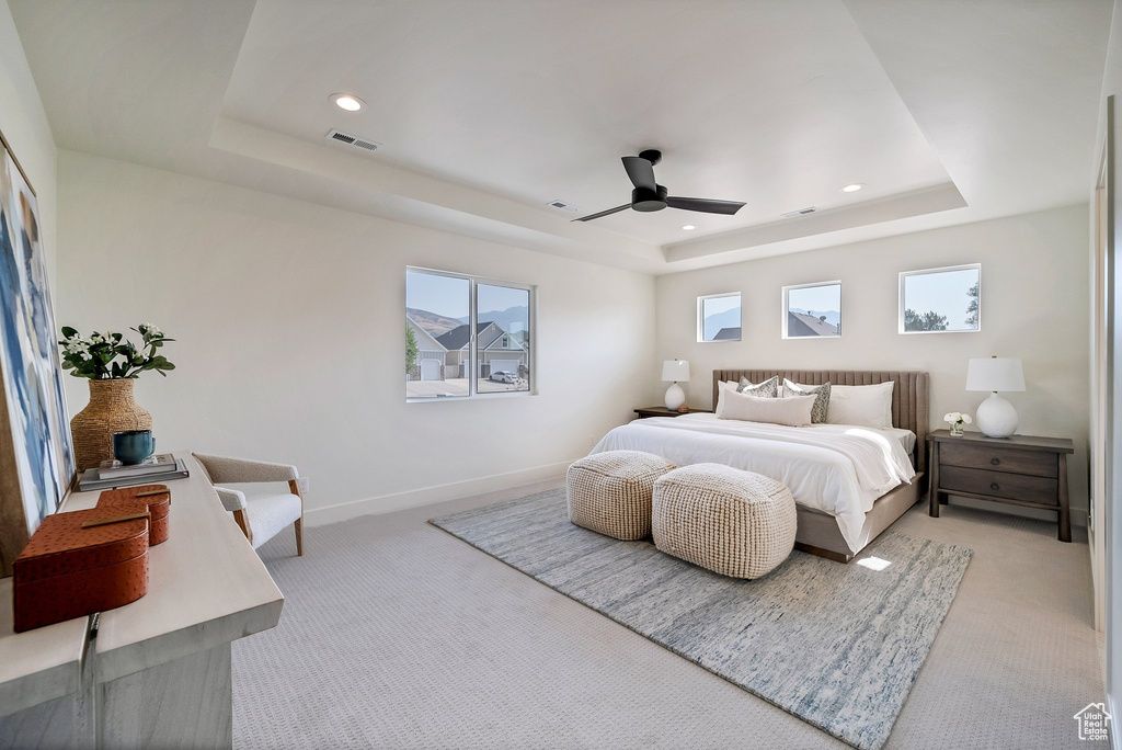 Carpeted bedroom featuring ceiling fan, multiple windows, and a tray ceiling