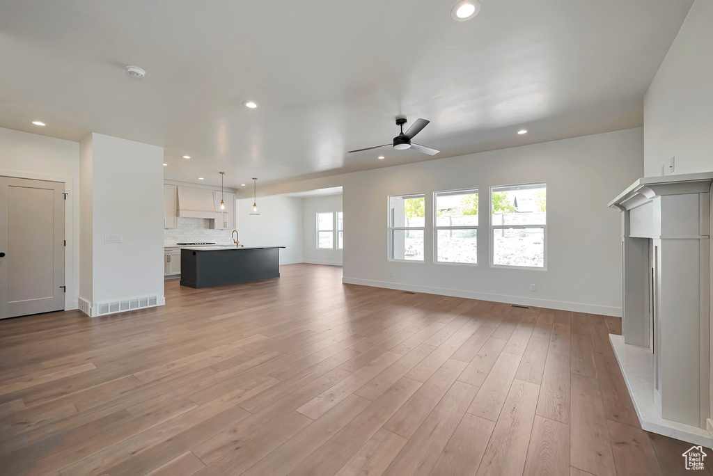 Unfurnished living room with sink, ceiling fan, and light hardwood / wood-style flooring