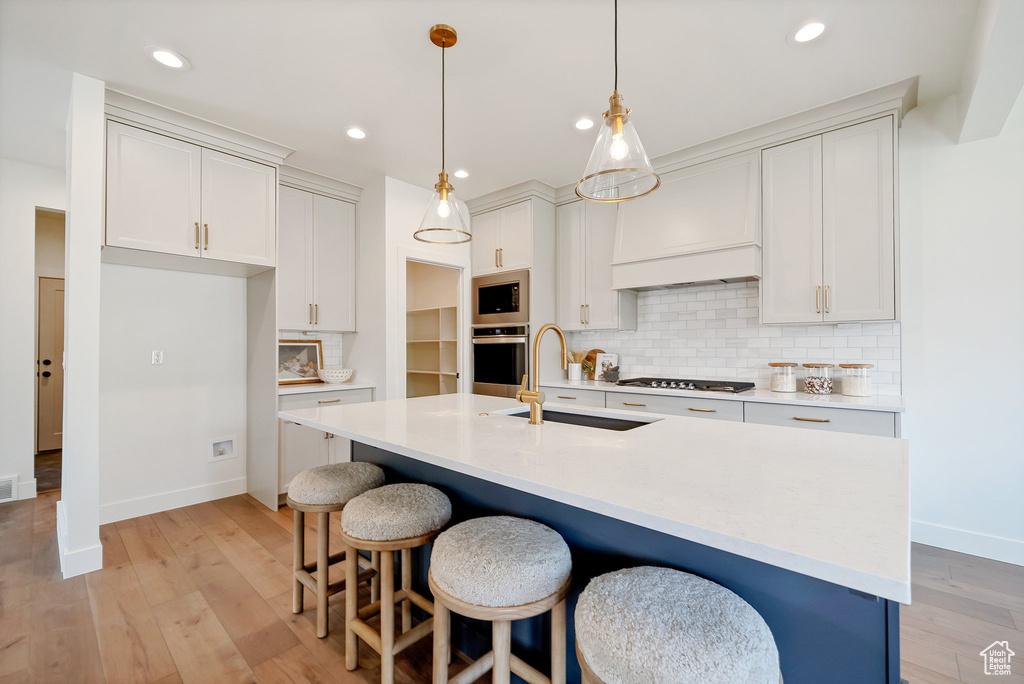 Kitchen with appliances with stainless steel finishes, decorative backsplash, sink, and light hardwood / wood-style floors