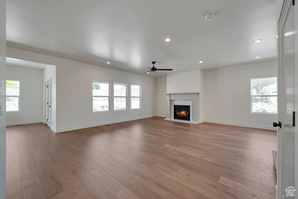 Unfurnished living room with a high end fireplace, ceiling fan, light hardwood / wood-style flooring, and a wealth of natural light