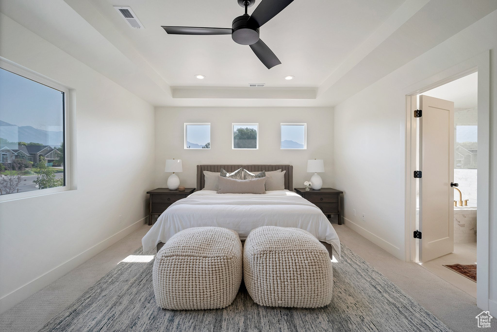 Bedroom featuring light carpet, multiple windows, and a tray ceiling