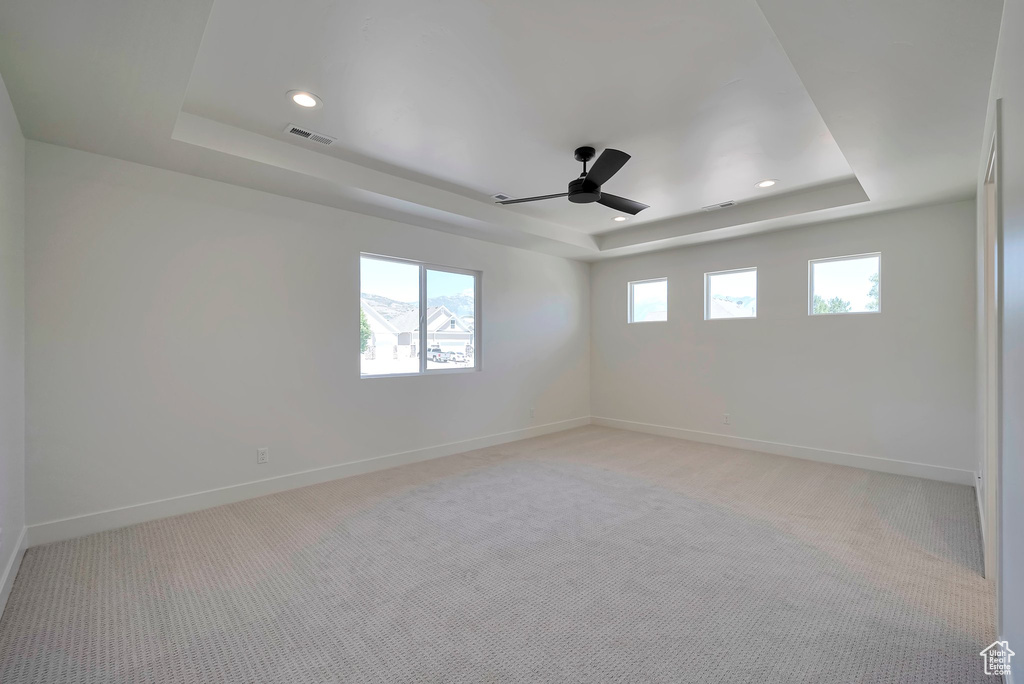 Empty room with carpet, ceiling fan, and a raised ceiling