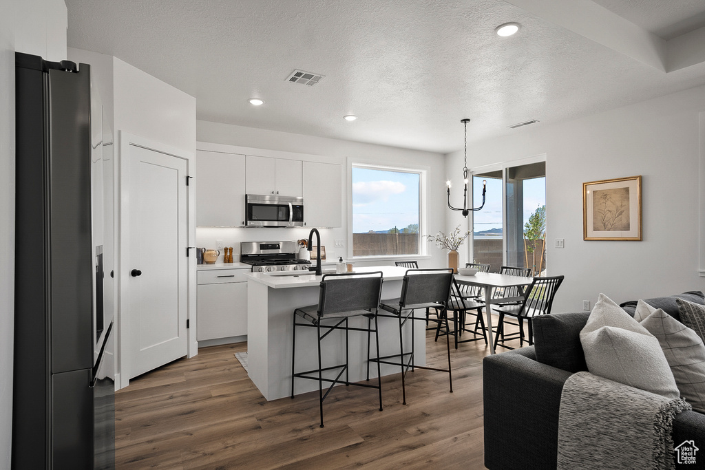 Kitchen featuring white cabinetry, a center island with sink, dark hardwood / wood-style flooring, stainless steel appliances, and decorative light fixtures