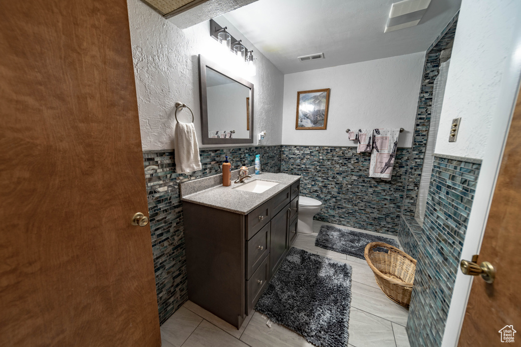 Bathroom with tile walls, backsplash, tile floors, toilet, and vanity