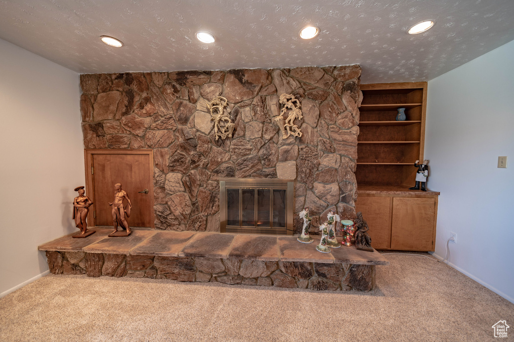 Unfurnished living room featuring carpet flooring, a stone fireplace, and a textured ceiling