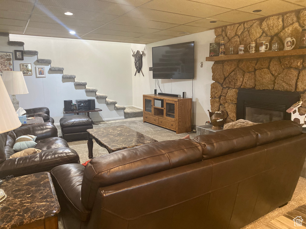 Living room with a stone fireplace, hardwood / wood-style flooring, and a drop ceiling