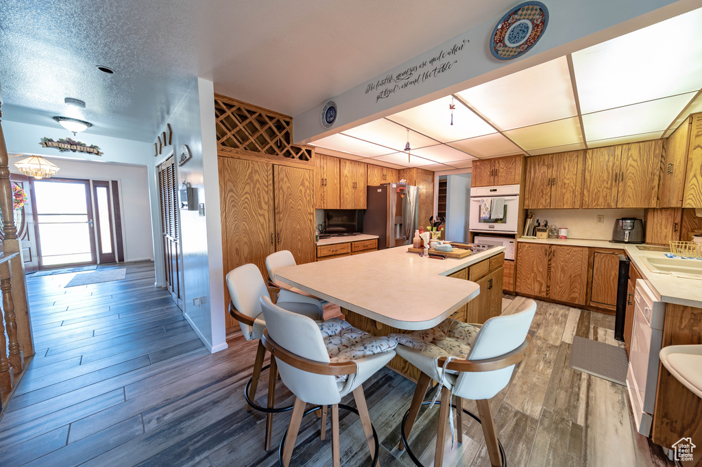 Kitchen featuring light hardwood / wood-style floors, a textured ceiling, wooden walls, a kitchen bar, and stainless steel fridge with ice dispenser