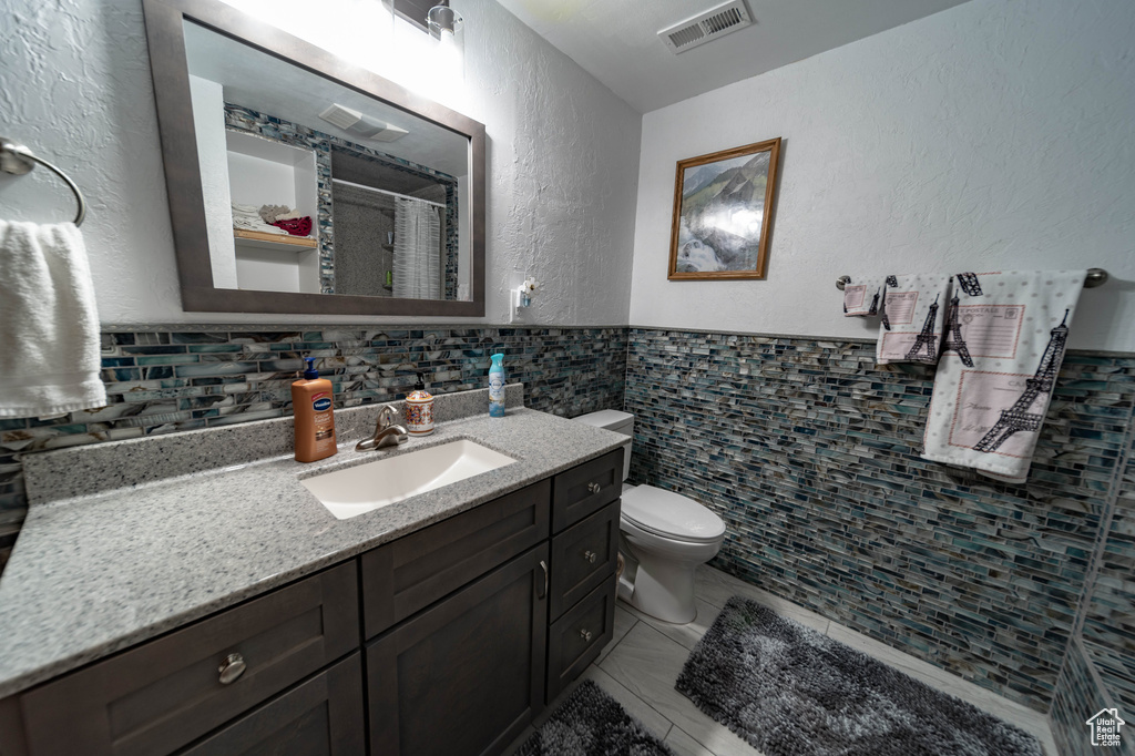 Bathroom featuring tile walls, vanity with extensive cabinet space, toilet, tasteful backsplash, and tile floors