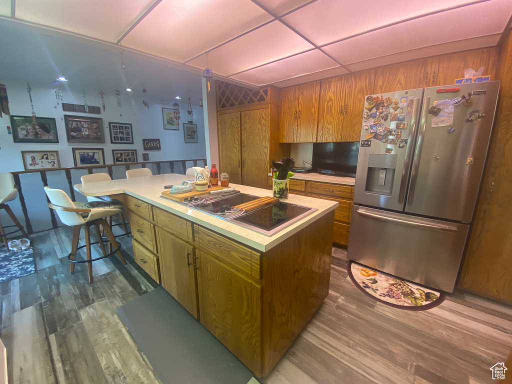 Kitchen with a center island, stainless steel fridge, black electric stovetop, a paneled ceiling, and wood-type flooring