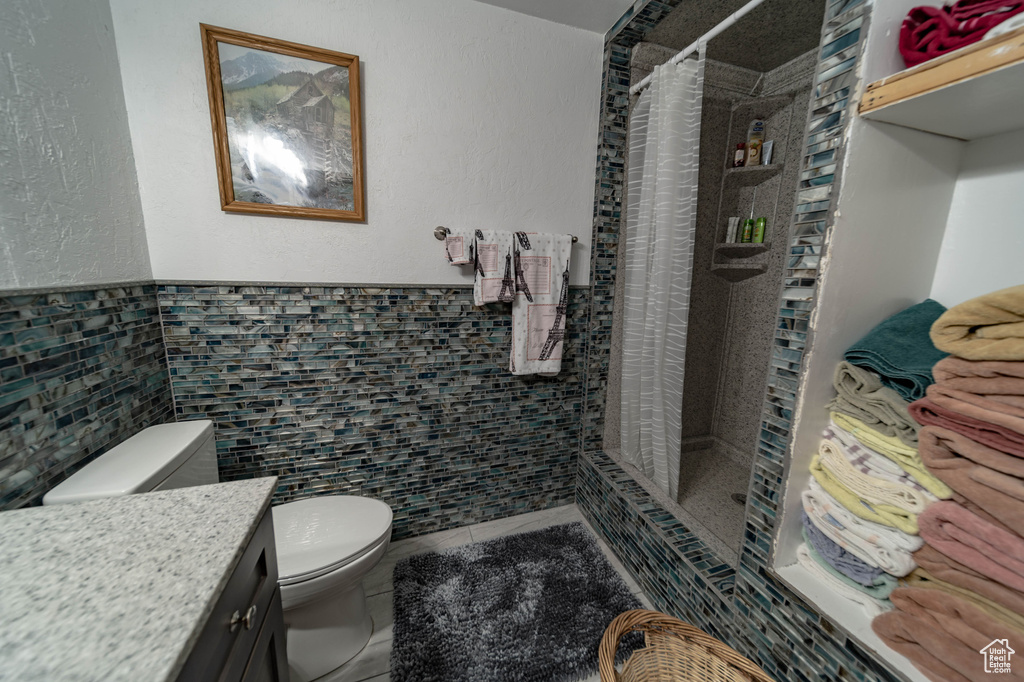 Bathroom with tile flooring, a shower with shower curtain, tile walls, vanity, and toilet