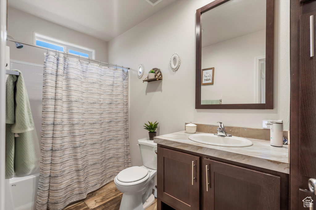 Full bathroom featuring hardwood / wood-style floors, shower / bath combo with shower curtain, toilet, and vanity