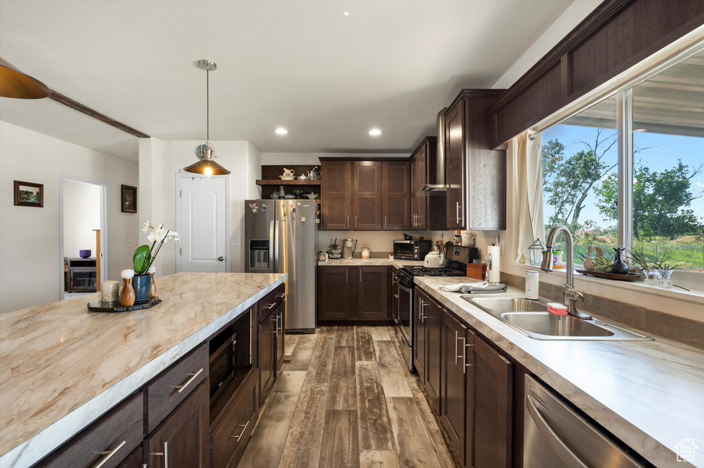 Kitchen with decorative light fixtures, stainless steel appliances, hardwood / wood-style floors, dark brown cabinets, and sink